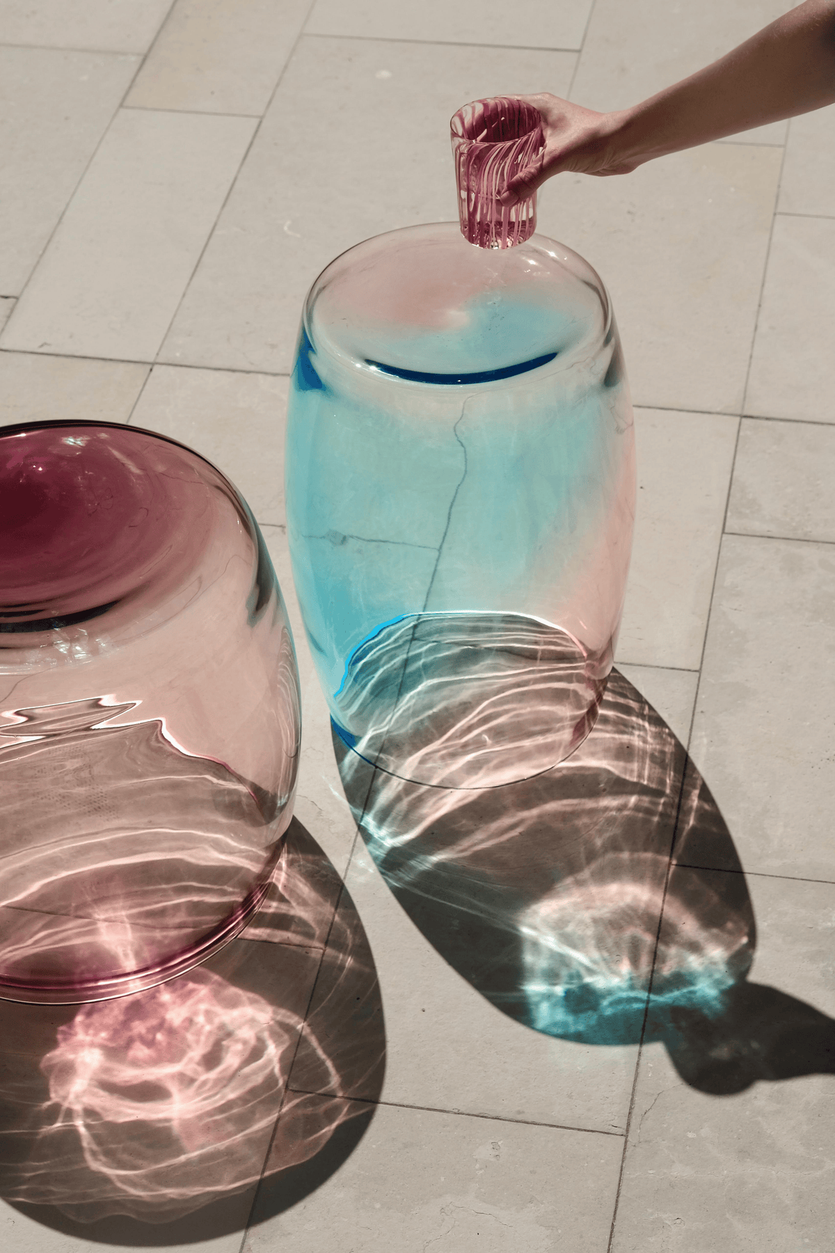 Murano glass Tavolini tables — Ametista 40 and Acqua Mare 40 — casting sculptural shadows and refracted light on pale stone flooring.