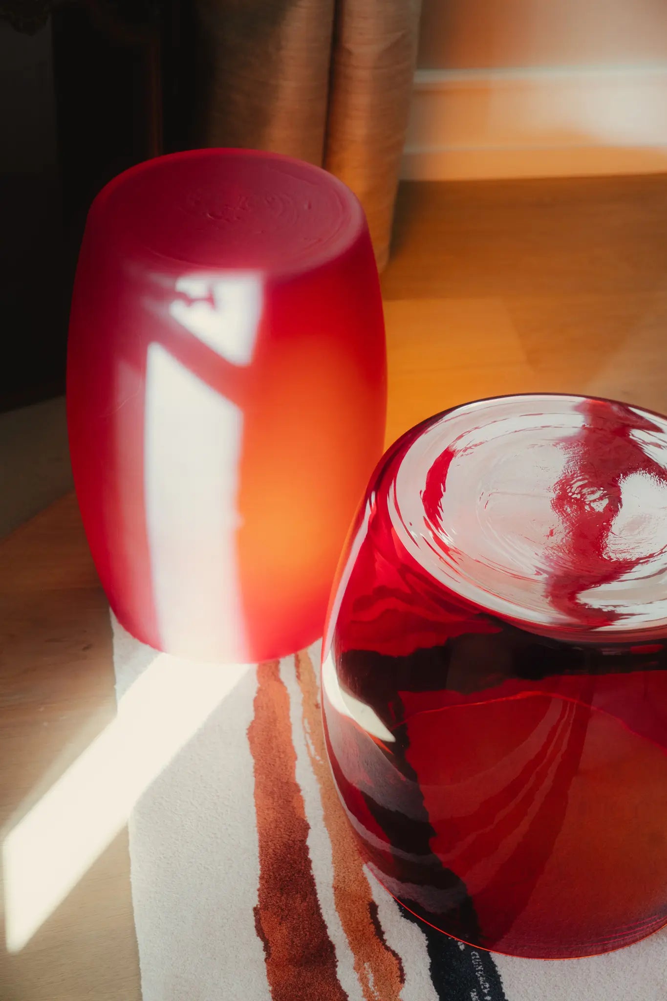   A pair of hand-blown Murano glass tables in deep ruby red hues, illuminated by warm sunlight on a textured rug.